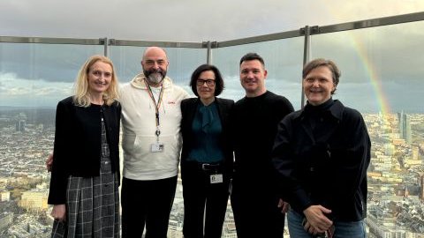 Foto von drei Frauen und zwei Männern auf Dachterrasse mit Regenbogen im Hintergrund