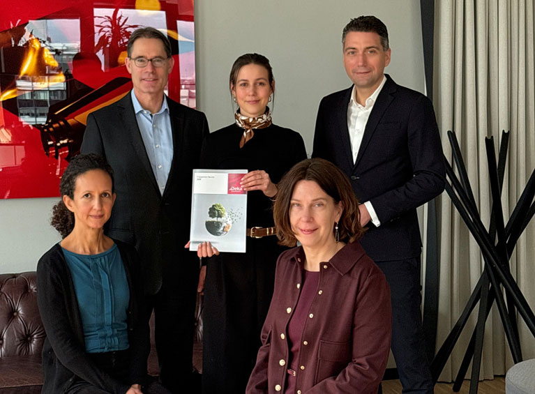 Drei Frauen und zwei Männer blicken in die Kamera, eine Frau hält den ausgedruckten Engagement-Bericht in der Hand