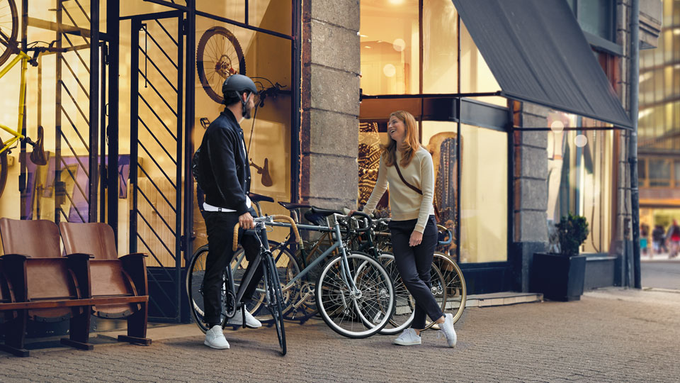 Mann mit Fahrrad und Helm und Frau unterhalten sich vor Fahrradgeschäft